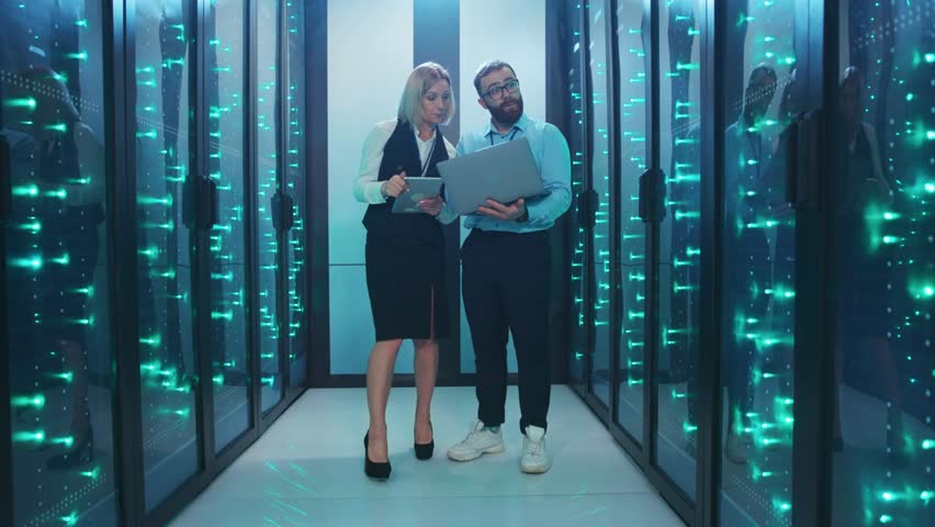 A man and woman work together in a server room, analyzing data - Powered by Shutterstock - Get 15% off with code: PIKWIZARD15