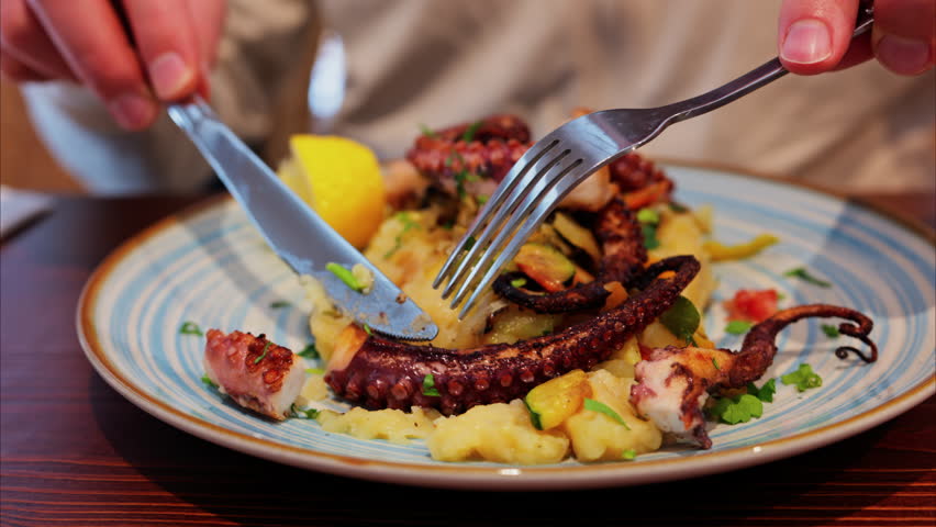 Close up of a man cutting and eating grilled octopus on a puree at a restaurant