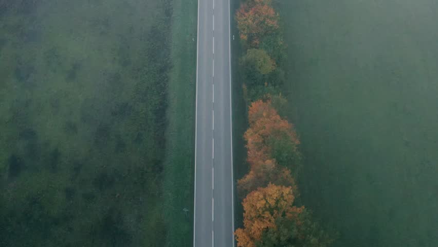 Drone aerial view, directly above, of a winding road going through nature on a cold morning day in autumn
