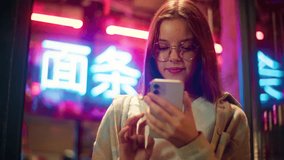Joyful Caucasian Asian teen child kid girl swipe mobile phone in neon city schoolgirl teenager scroll social media feed night junior Internet. The inscription noodle in Chinese. Translation: 'noodle'. - Powered by Shutterstock - Get 15% off with code: PIKWIZARD15