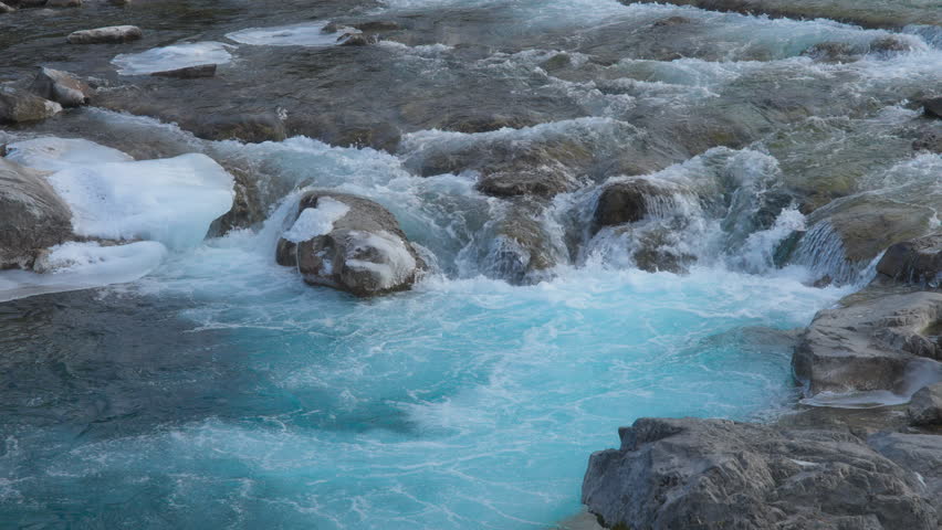 Turquoise water flowing between the rocks in the river. Slow motion.