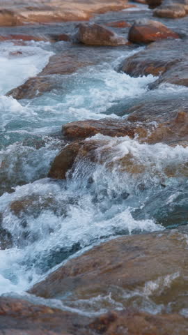 Stream of water flowing down the rocks. Slow motion. Vertical Format.
