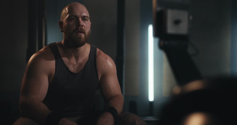A strong man in a tank top sits and rests during a break between sets during a fitness and sports class in a modern gym