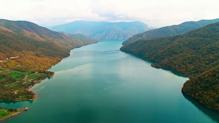 A drone view of the river in the woods. An aerial view of an autumn forest. Winding river among the trees. Turquoise mountain water. Landscape with soft light before sunset. Georgia, Ananuri Mountains