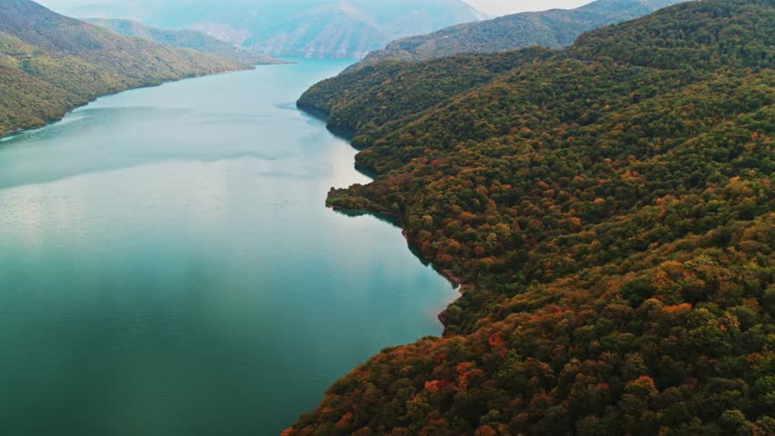 A drone view of the river in the woods. An aerial view of an autumn forest. Winding river among the trees. Turquoise mountain water. Landscape with soft light before sunset. Georgia, Ananuri Mountains