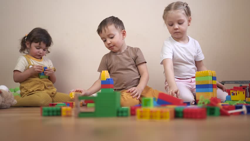 Three children playing with blocks. Children play together in a group. Build a new floor for your kindergarten with toys and a constructor. Three kids engaging with building lifestyle blocks.
