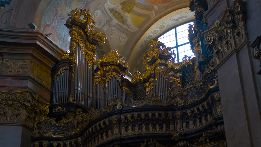 Vienna, Austria, September 15, 2024. Ornate church organ. Golden light streaming through a high arched window illuminates an intricately carved church organ, showcasing ornate details
