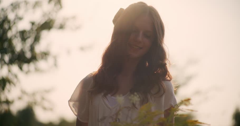 Happy little girl with dreamy expression holding wildflowers in warm sunset light