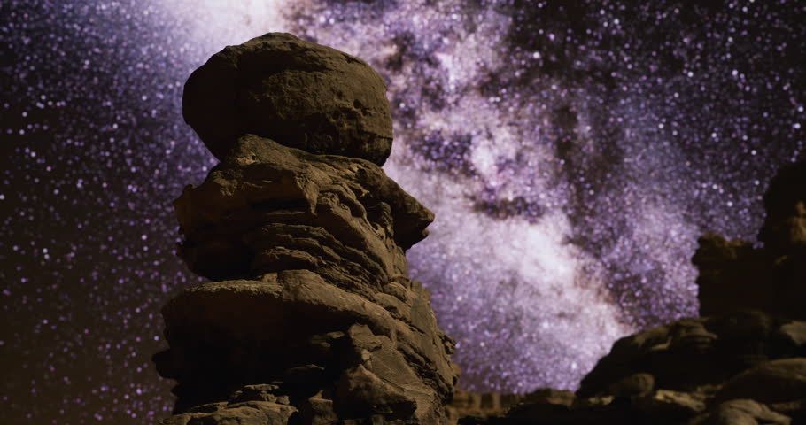 A majestic rock formation stands prominently against a brilliantly lit night sky filled with stars and the Milky Way, creating a breathtaking natural spectacle at a remote site.