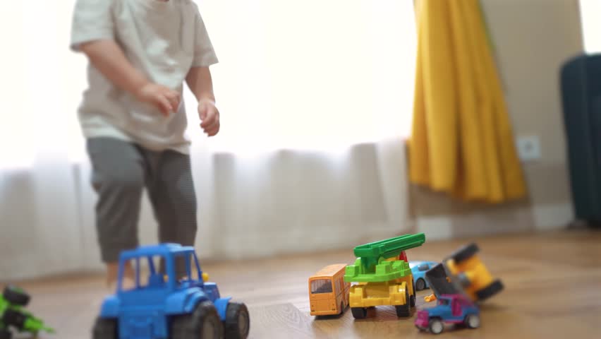 Young child playing with toy trucks. Child is rolling a toy on a tractor. Close up of family playing a game at home. A small child enjoying playing with toy trucks lifestyle.