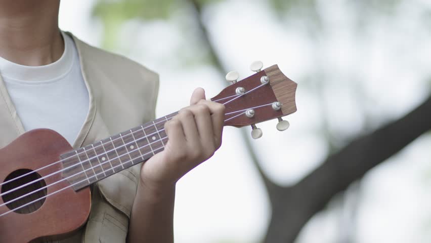 A boy is playing the ukulele in the garden.
