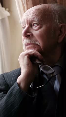 Old grandfather calmly looks out the window, immersed in nostalgia