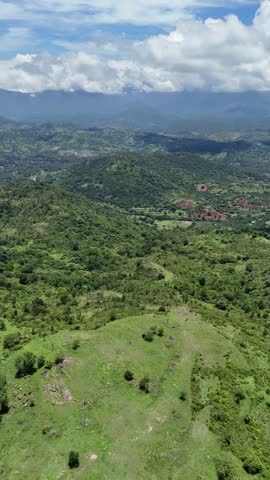 A scenic view of a lush green mountain range partially covered by white clouds, set against a deep blue sky. The misty clouds add a mystical touch to the natural landscape.