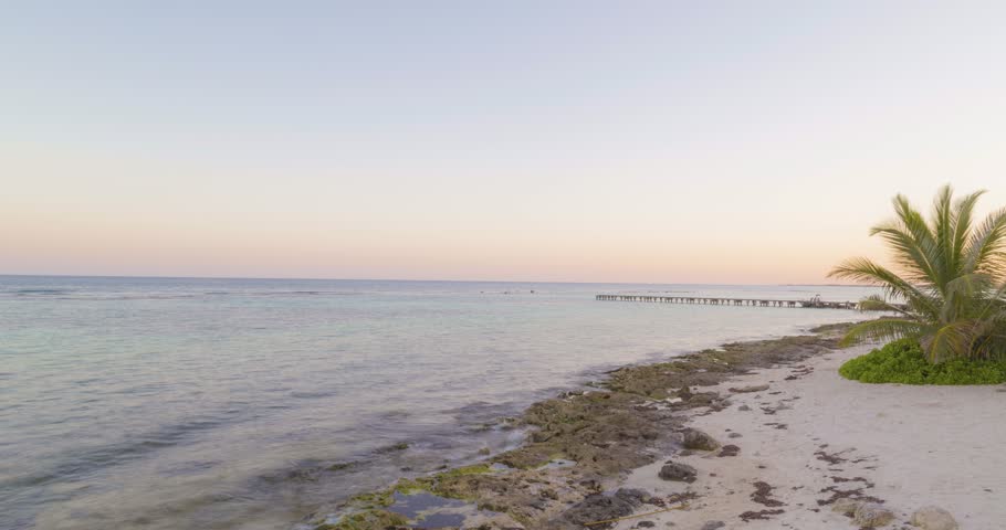 Calm turquoise waters lap against the shore as the sky glows with pastel hues during a breathtaking sunset in tulum, mexico