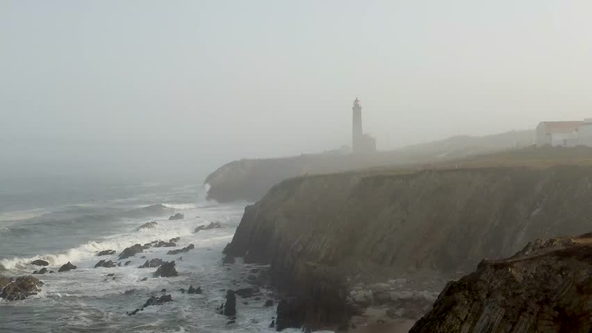 Misty lighthouse standing on dramatic Portugal coastline at dawn