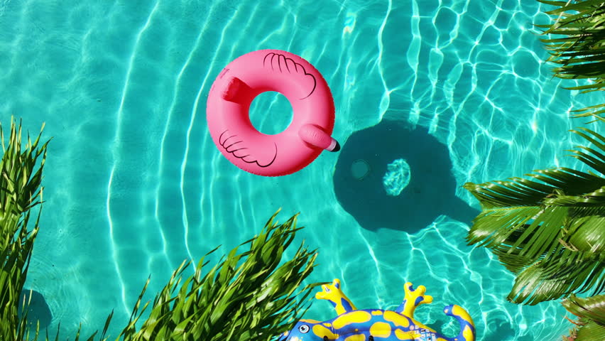 Top down summer vacation background. Aerial view clear blue pool with a pink inflatable Flamingo ring, surrounded by green palm trees. Florida holidays, Miami luxury trip, Hotel destination 4k copy