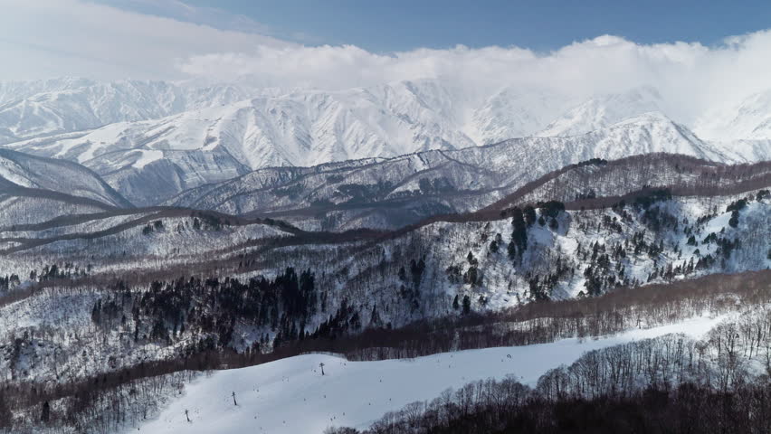High-angle shot of snowy mountain range with trees under a blue sky in Nagano, Japan