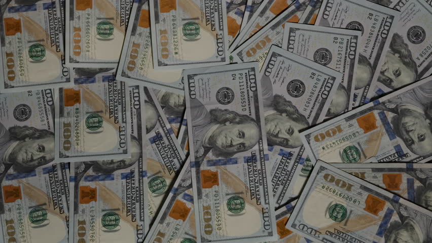 Hundred-dollar bills scatter and fly out of the frame, leaving only three remaining on the table against a dark background, symbolizing dwindling wealth or loss