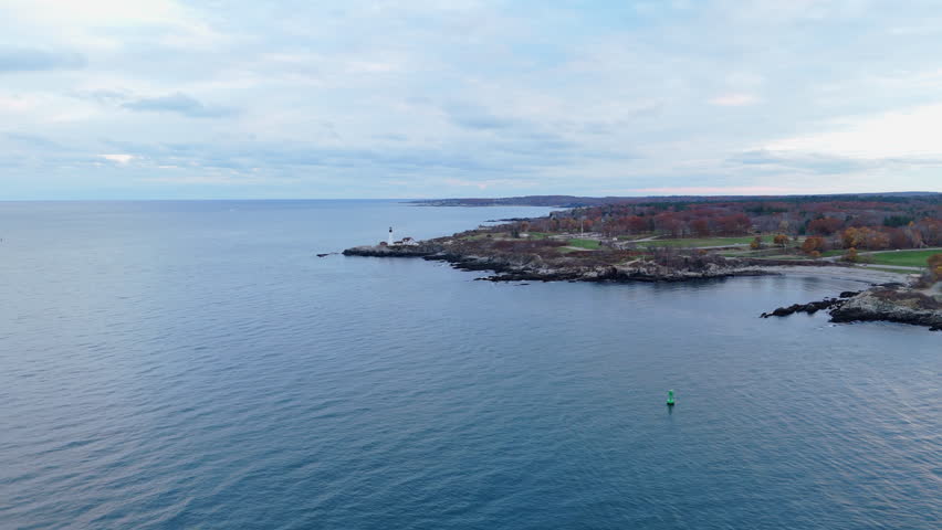 A breathtaking aerial drone photograph captures the iconic Cape Elizabeth Lighthouse during a stunning sunset, beautifully showcasing the picturesque coastline and tranquil waters of Portland, Maine