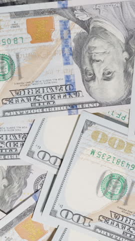 Vertical video. Throwing and taking back a large wad of hundred-dollar bills in an active motion, displayed over a spread of scattered currency in a financial-themed composition