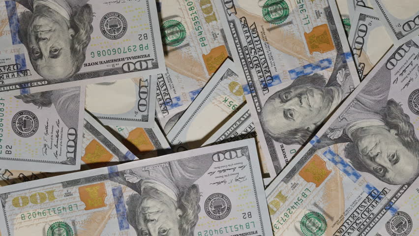 A close-up slider view gliding smoothly over scattered hundred-dollar bills, capturing intricate details of the notes' design and texture