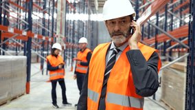 Warehouse manager wearing safety vest and helmet talking on mobile phone, coordinating logistics and operations - Powered by Shutterstock - Get 15% off with code: PIKWIZARD15