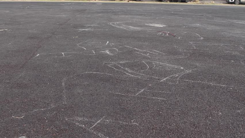 Little girl in pink rollerblades slowly skates left on rubber ground covered with chalk drawings, learning to move with effort in 4k video