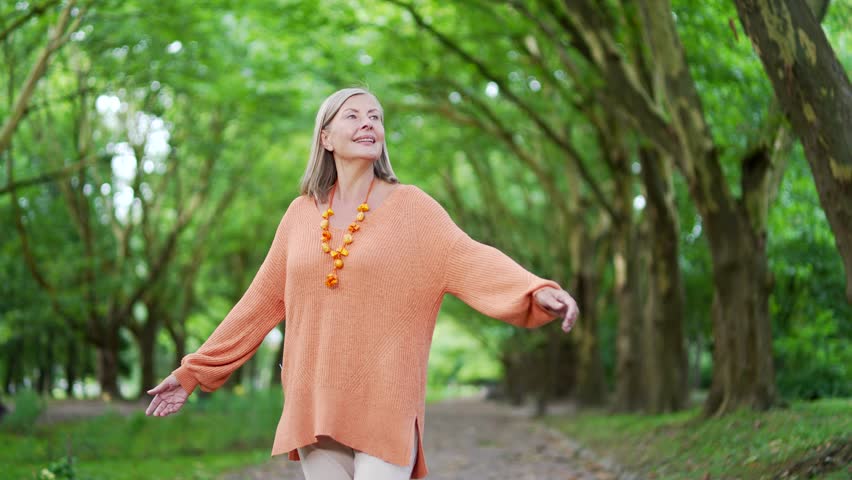 Happy mature female with gray hair dancing circling walking in urban city park, expressing joy and freedom spending leisure time outdoors. Elderly woman enjoying walk with mood of happiness. Close up - Powered by Shutterstock - Get 15% off with code: PIKWIZARD15