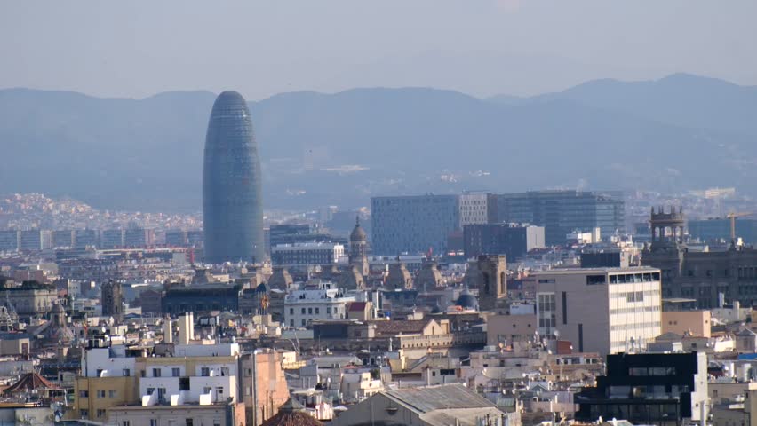 Hazy Barcelona cityscape panorama featuring the prominent landmark and distant mountains.	