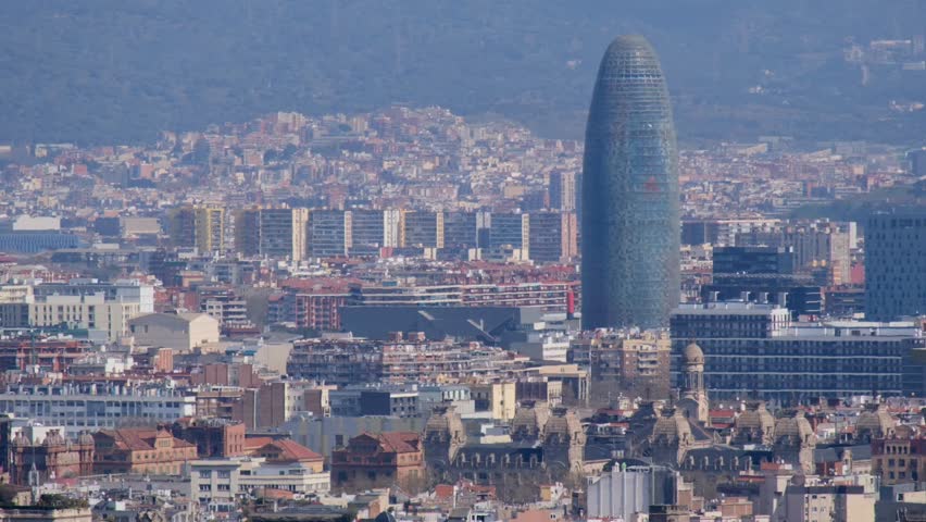 Hazy Barcelona cityscape panorama featuring the prominent landmark and distant mountains.	