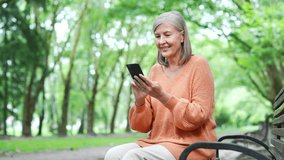 Older woman using phone outdoors while sitting on bench in urban city park, enjoying leisure time. Elderly female texting, chatting online, browsing the web, reads writes messages on a smartphone - Powered by Shutterstock - Get 15% off with code: PIKWIZARD15