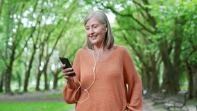 Mature woman enjoying walk outdoors using phone with earphones in urban city park, embracing active lifestyle and technology. A happy elderly female is walking listening to music on a smartphone - Powered by Shutterstock - Get 15% off with code: PIKWIZARD15