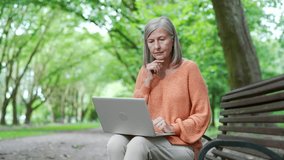 Elderly woman sitting on bench, using laptop in park. Thoughtful elderly female with gray hair typing on computer, working in application, texting, chatting online, browsing web, reads writes messages - Powered by Shutterstock - Get 15% off with code: PIKWIZARD15