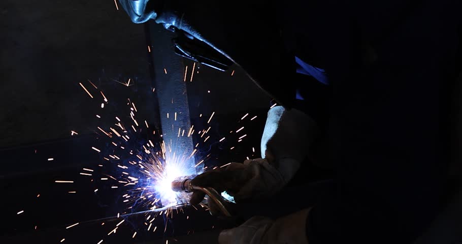 Welder at work in metal industry, welding metal construction - slow motion. Close-up shot lots of sparks in the factory