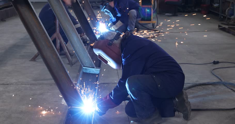Workers welding and grinding metal construction in metal industry - slow motion. Lots of sparks in the factory