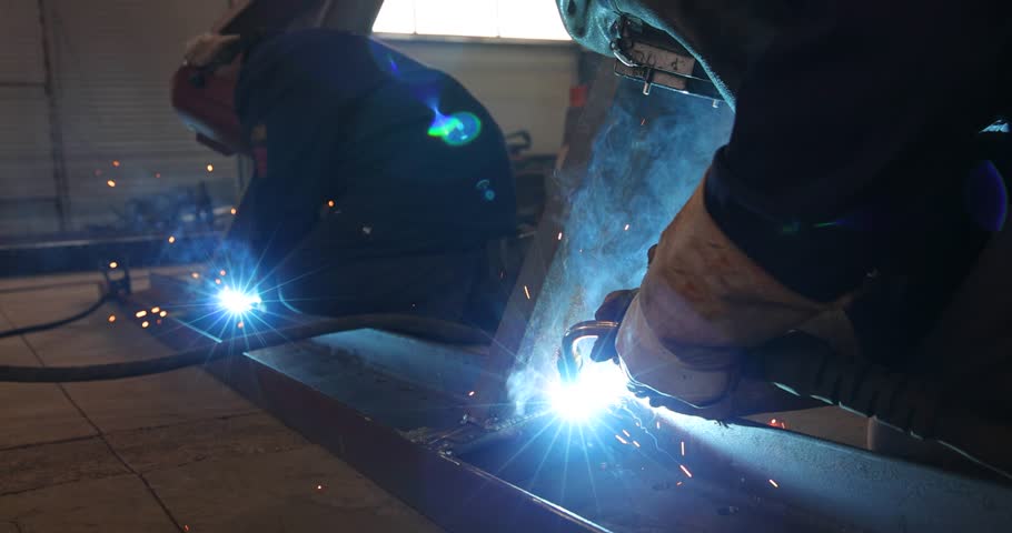 Welders at work in metal industry, welding metal construction - slow motion. Close-up shot lots of sparks in the factory
