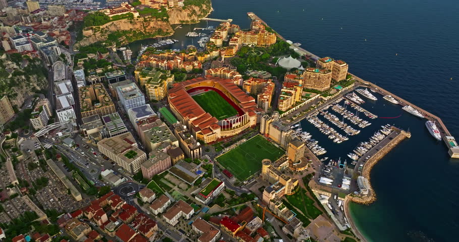 Aerial view of the city center of Monaco. Establishing shot showcases luxury yachts moored in Monaco Bay, the Palais Princier de Monaco, and luxury apartment buildings of Monte Carlo