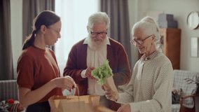 Young woman unpacking fresh groceries from paper bag for grateful senior grandparents at home, elderly man checking shopping list on smartphone - Powered by Shutterstock - Get 15% off with code: PIKWIZARD15