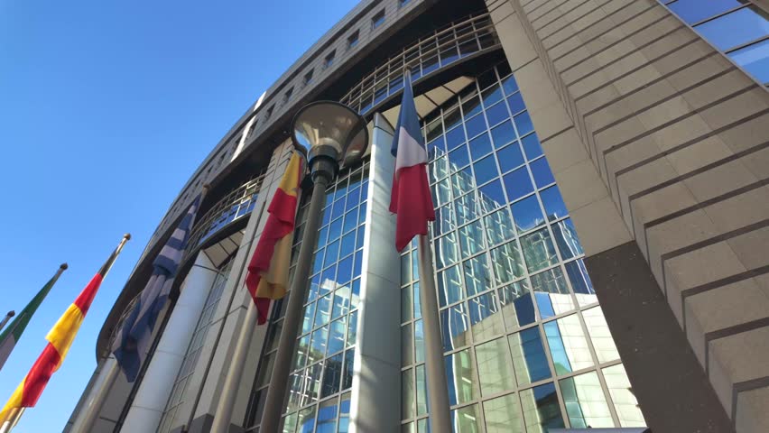 Ukrainian flag waving outside modern glass facade of European Parliament