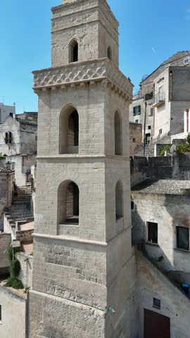 Bell tower of the ancient church of San Pietro Barisano in Matera, southern Italy, with clear sky. Vertical video by drone in 4k. Sassi di Matera, history and culture.