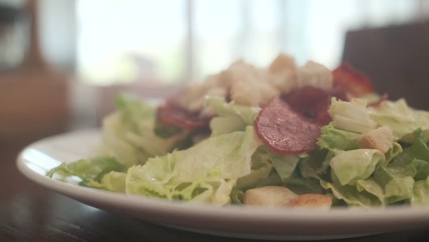 Traditional caesar salad in a white bowl with leaves and a sauce boat and parmesan. Selected focus.