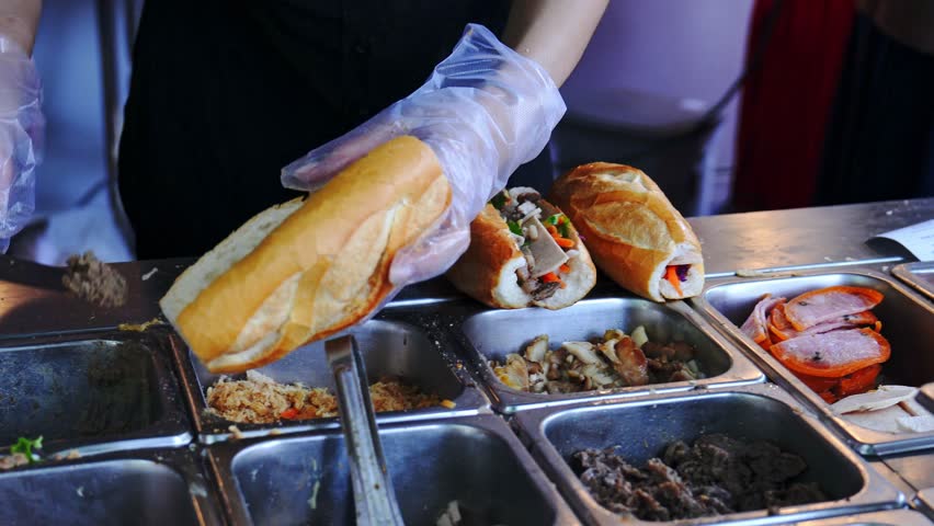 Female chef serving traditional vietnamese sandwich Banh Mi in street food with meats, pork roll and vegetables. It combines Vietnamese cuisine with French condiments like pate