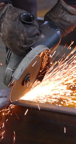 Steel worker grinding a metal construction with grinder in the factory, close up slow motion