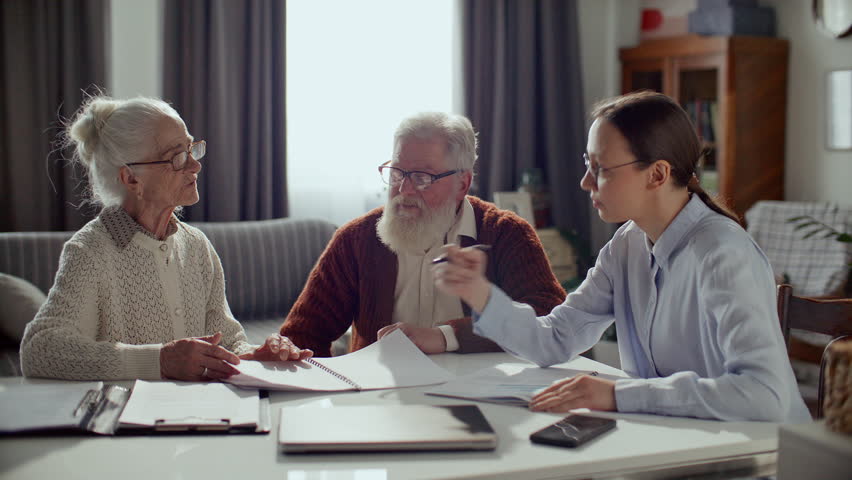 Female financial consultant reviewing documents with elderly couple, explaining savings plan and providing professional advice during meeting at home