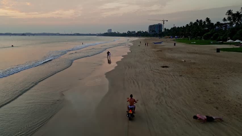 Man driving moto along ocean beach at sunset. Aerial view back opening