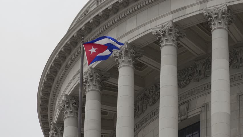 Cuban flag waving in wind at building of Capitol in Havana, Cuba, cloudy weather, almost black and white background, colourful flag