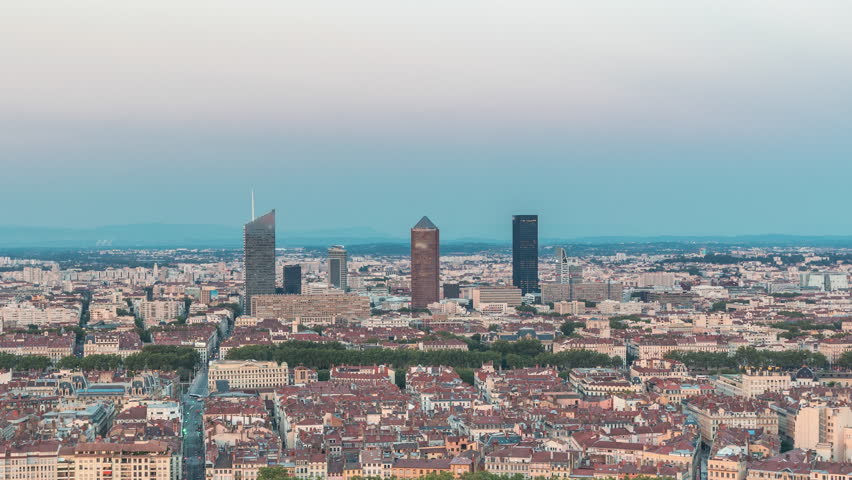 Panoramic aerial view of Lyon after sunset from Fourviere Hill day to night transition. The skyline features Rhone River and iconic city landmarks illuminated in warm evening