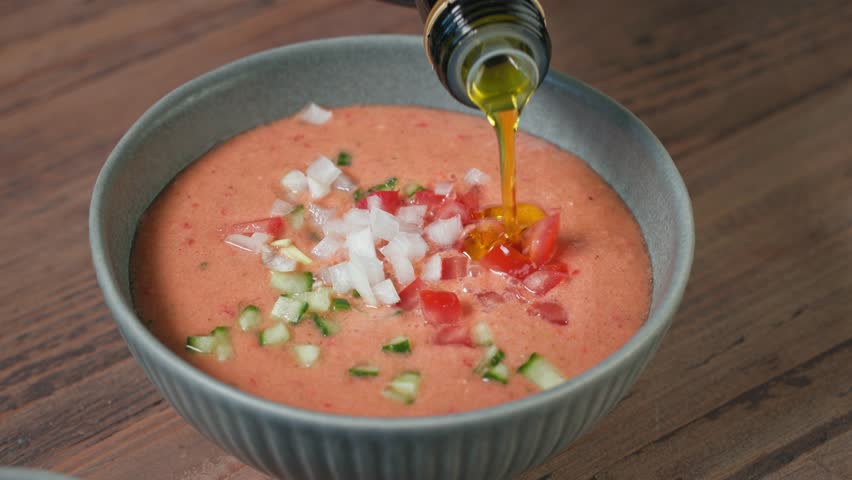 cook add olive oil in a bowl of gazpacho, process of making fresh cold tomato soup. food closeup