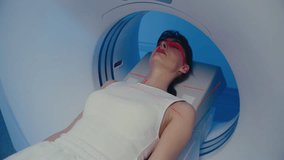 Pretty woman lying motionless inside MRI scanner while red positioning lasers crossing her face and chest. Patient keeping eyes closed and breathing calmly during imaging process at hospital. - Powered by Shutterstock - Get 15% off with code: PIKWIZARD15