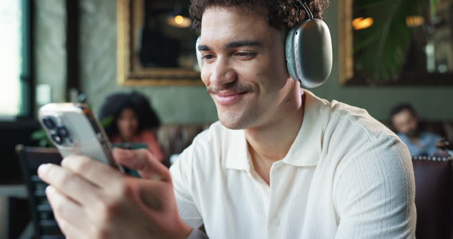 Headphones, relax and man in coffee shop with phone listening to music, radio and playlist. Restaurant, happy and person on smartphone for internet, streaming and audio subscription on break in cafe